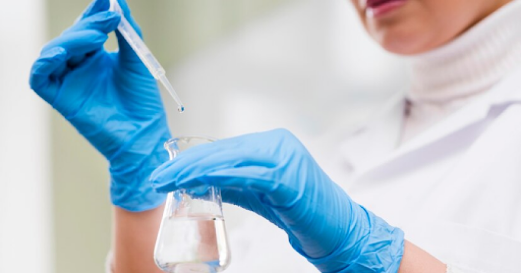 A female scientist in a lab coat carefully holds a test tube