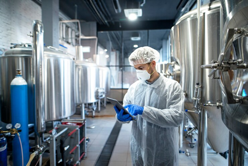 Technologist in white protective uniform controlling industrial process using tablet device